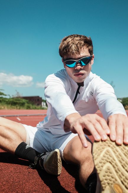 A young athlete in sunglasses stretches on an outdoor track under clear skies, embodying fitness and determination.