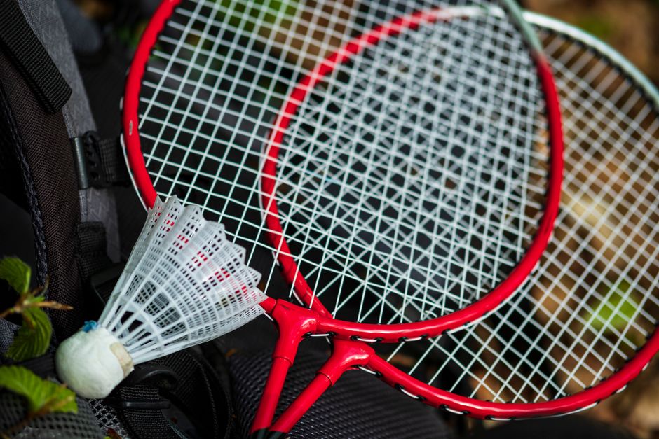 Two red badminton rackets and a shuttlecock on a backpack outdoors, perfect for leisure and sports activities.