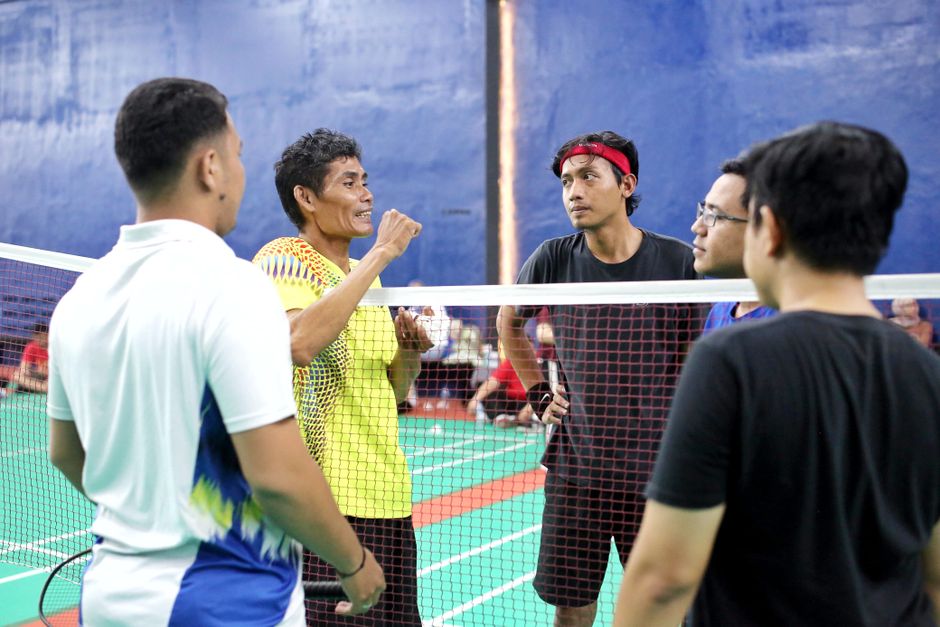 A group of men discussing strategy on an indoor badminton court.