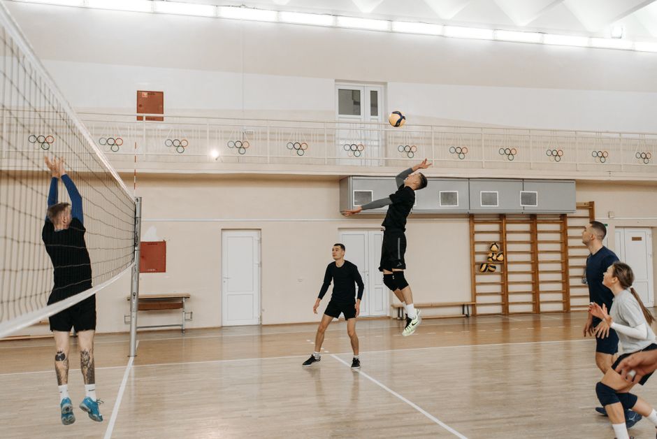 Competitive indoor volleyball match with athletes spiking the ball over the net.