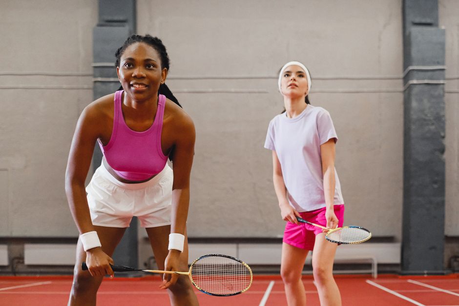 Two women playing badminton indoors, focusing on a competitive moment.