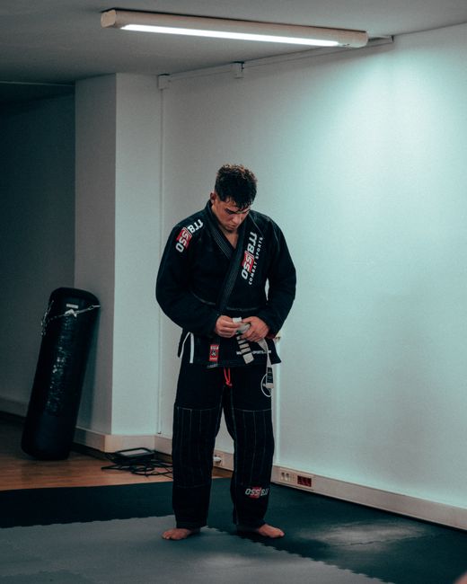 Martial artist tying belt, preparing for training in an indoor gym environment.