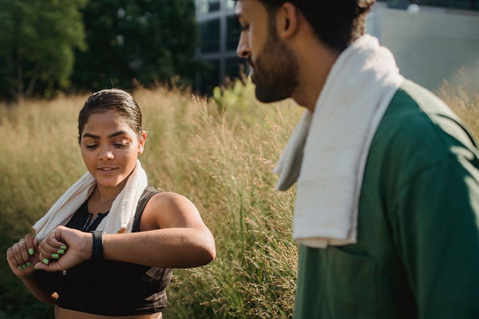 A couple outdoors using fitness trackers after a workout, wearing towels.