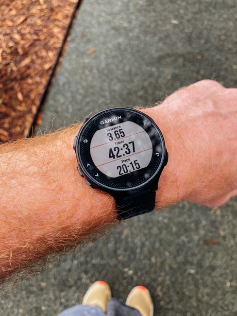 Close-up of a smartwatch showing running distance, time, and pace on a wrist outdoors.