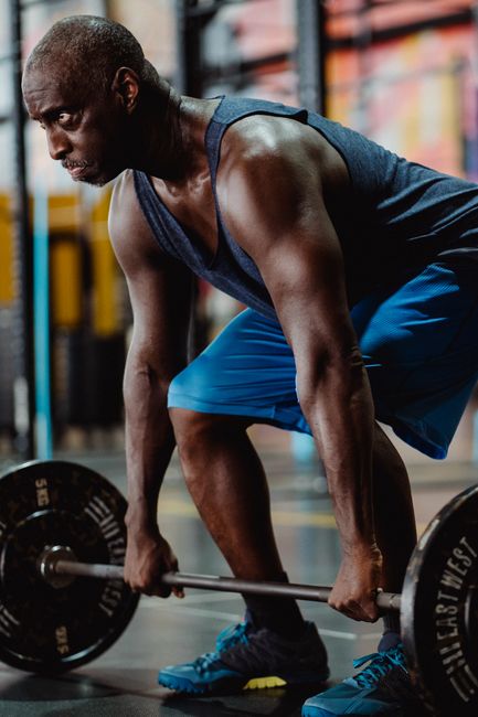 A muscular adult lifting weights in a modern gym setting, showcasing strength and focus.