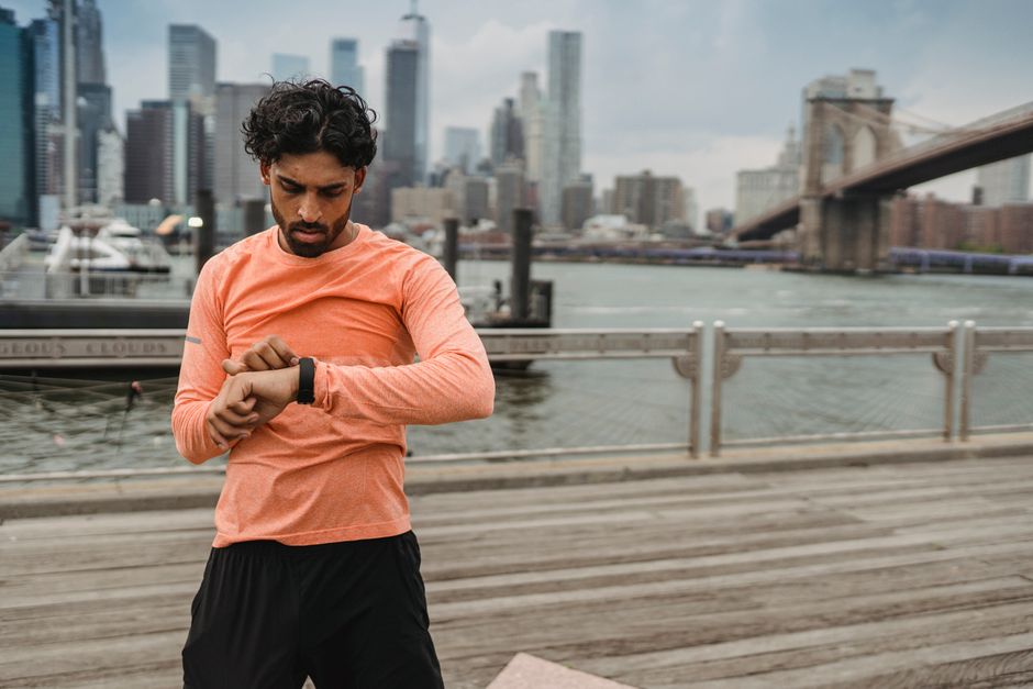 Adult man checks smartwatch while exercising by the Brooklyn Bridge, promoting healthy lifestyle.