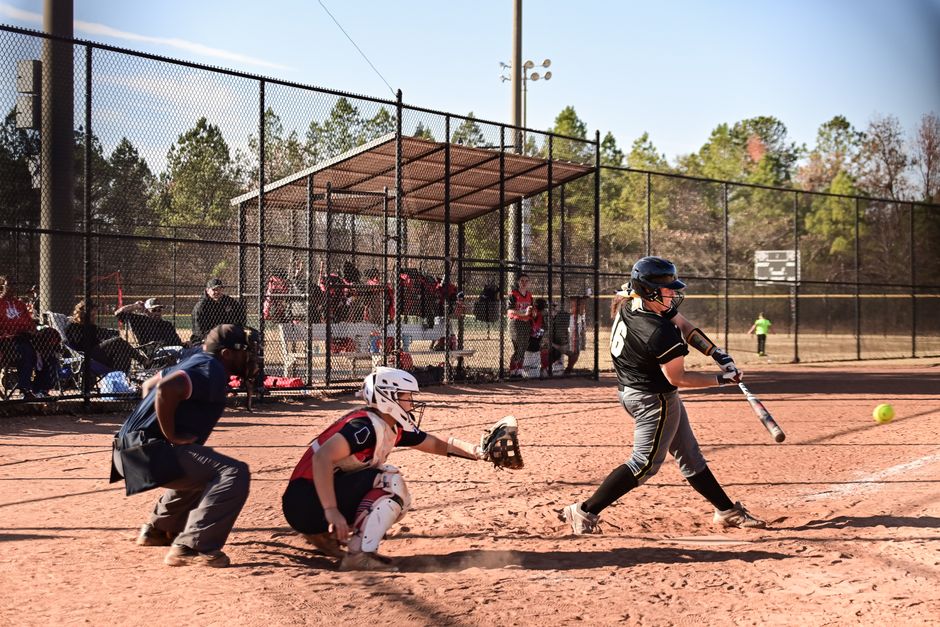 A thrilling moment in a softball game as the batter swings at a pitch on a sunny day.