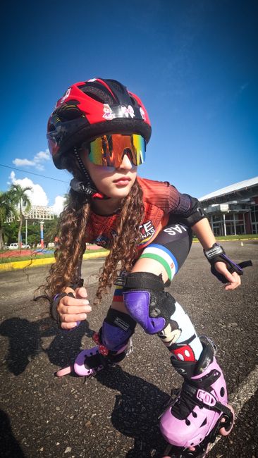 Young girl roller skating wearing protective helmet and knee pads for safety outdoors.