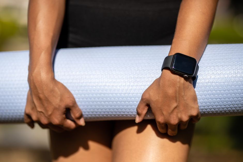 Close-up of hands holding a yoga mat, wearing a smartwatch, showcasing fitness lifestyle.
