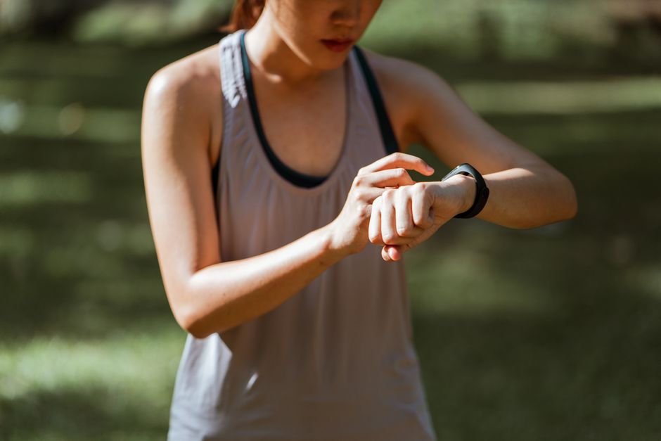 Crop focused sportswoman wearing activewear checking information on contemporary wrist fitness bracelet while exercising in sunny summer park