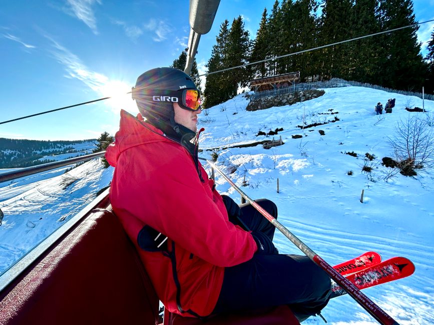 A skier in vibrant clothing relaxes on a ski lift with snowy mountains in Tyrol, Austria.