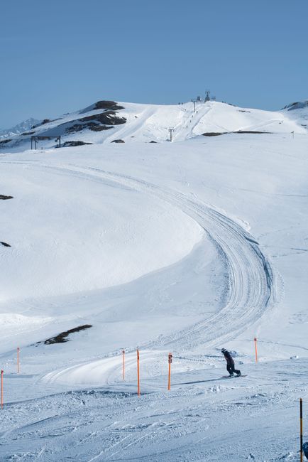 Snowboarder carving down a snowy slope at a ski resort under a clear blue sky.