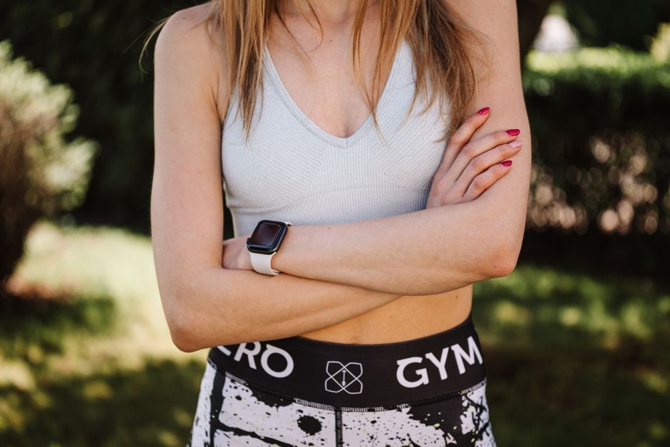 Confident woman in a sports bra and leggings, arms crossed, outdoors.