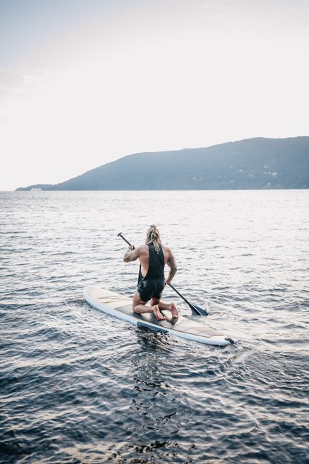 A man paddleboards across calm ocean waters near a scenic coastline under a bright sky.