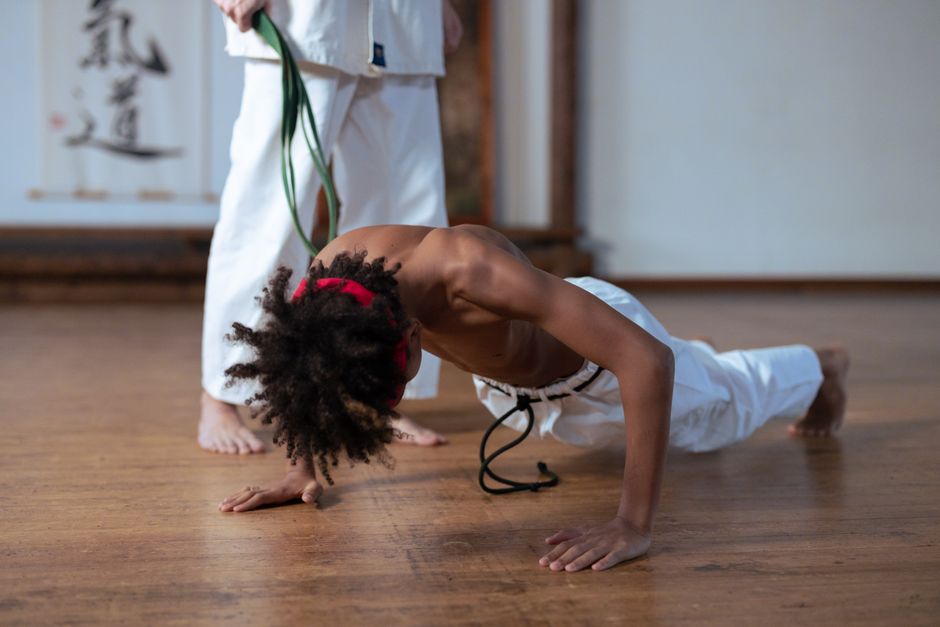 A boy practicing push-ups in a martial arts class, guided by a trainer.