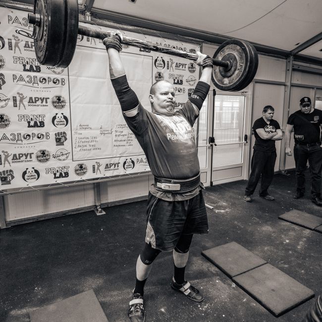 A strong man lifting a barbell in an indoor gym setting, showcasing strength and determination.