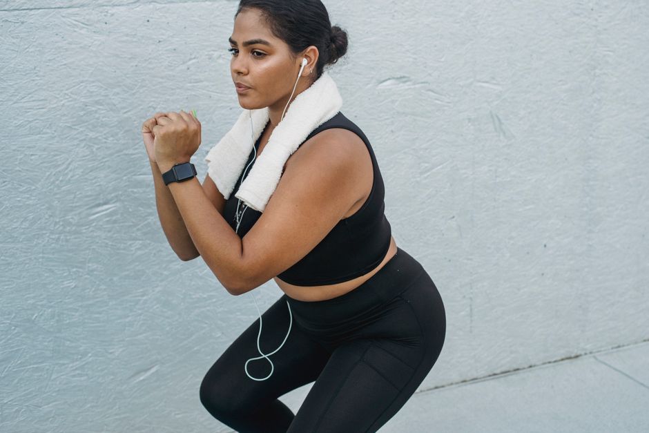 Fit woman exercising outdoors with headphones, towel, and fitness tracker, showcasing a healthy lifestyle.