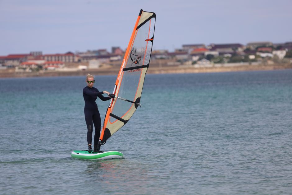 Woman enjoying windsurfing on a sunny day near a coastal village.