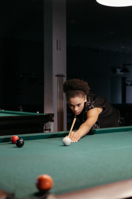 Focused woman with afro hair playing billiards indoors.