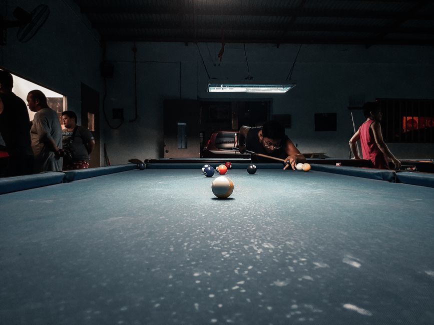 Focus on a billiards game with players aiming skillfully in an intimate indoor setting.