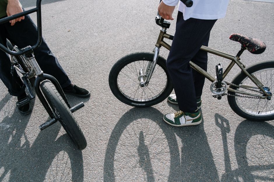 Two people with BMX bikes in an outdoor skatepark scene.