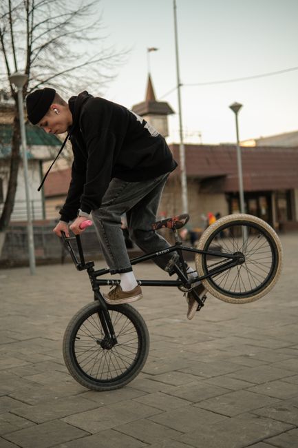 A young man skillfully performs BMX stunts on a pavement in an urban area, showcasing balance and control.