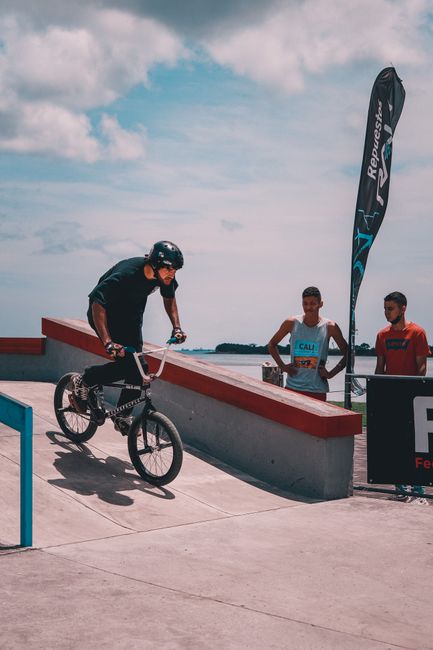A BMX rider performs a stunt on a skatepark ramp with onlookers nearby, capturing a dynamic outdoor scene.