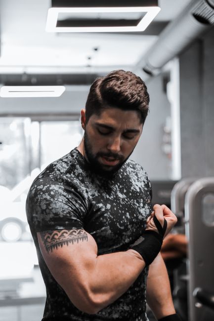 A strong, muscular man flexes his biceps in a gym with modern equipment.