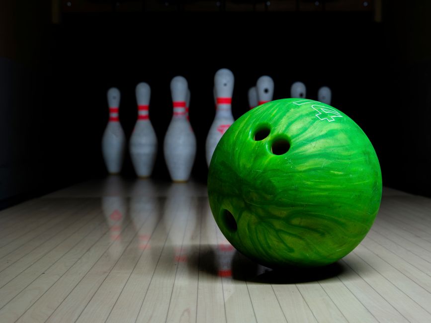 Close-up of a green bowling ball with pins ready to be knocked down.