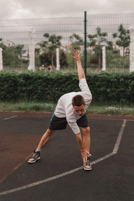 A man performs stretching exercises on an outdoor basketball court, promoting fitness and healthy living.
