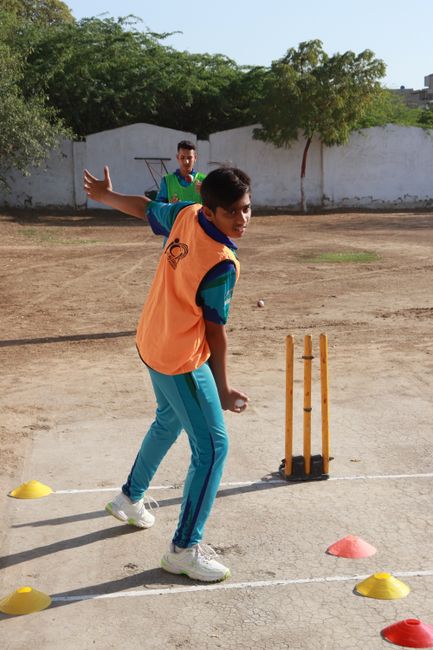 Young boys practicing cricket bowling drills outdoors on a sunny day.