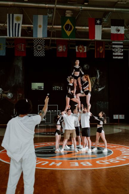 A cheerleading team executing a complex stunt on an indoor basketball court, captured in motion.