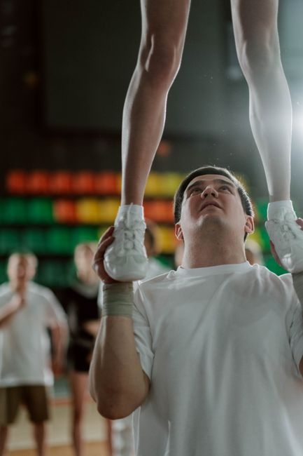 A cheerleader supported by a teammate during practice in a sports hall.