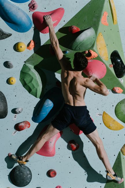 Muscular man showcasing strength and agility while climbing a colorful indoor rock wall.