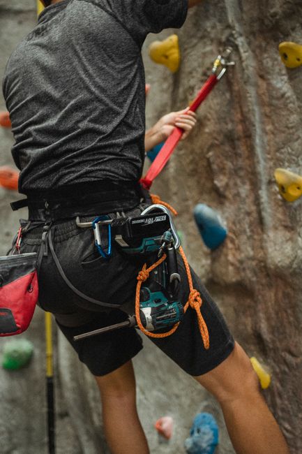 Back view of crop unrecognizable repairman in activewear and safety belt hanging near climbing wall before fixing with screwdriver