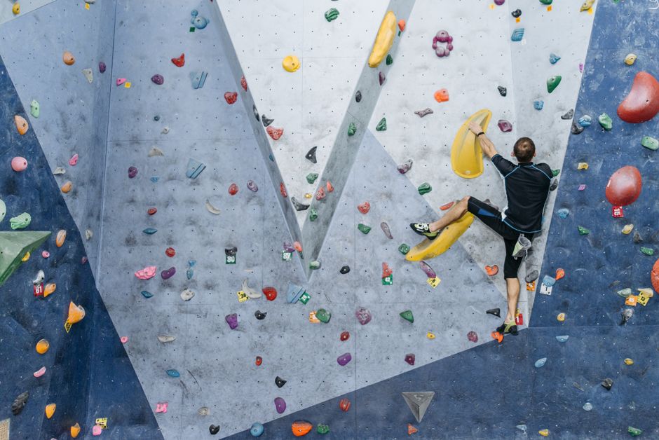 A man in activewear climbing an indoor bouldering wall with colorful holds.