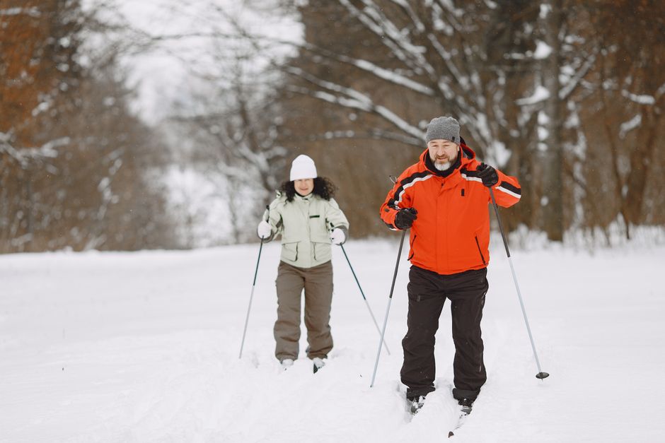 A man and a woman skiing through a snowy forest, enjoying a winter outing in warm clothing.