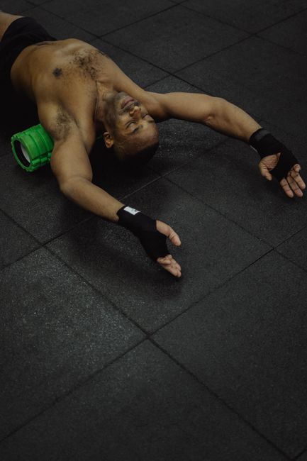 Shirtless African American man using a green foam roller for muscle relaxation and recovery.