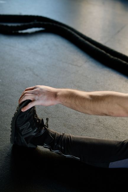 An athlete stretches on the gym floor, preparing for a workout with battle ropes in the background.
