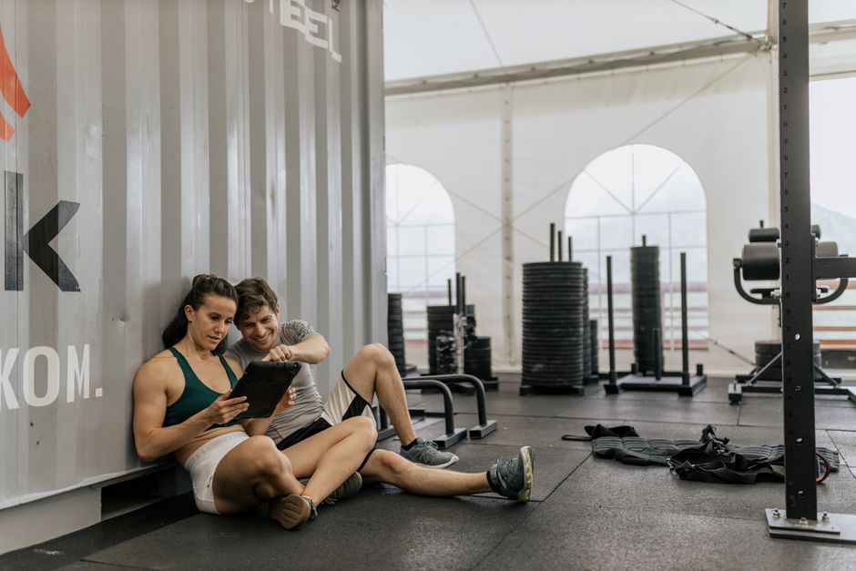 A young couple sitting on the gym floor, using a tablet in a modern urban fitness center.
