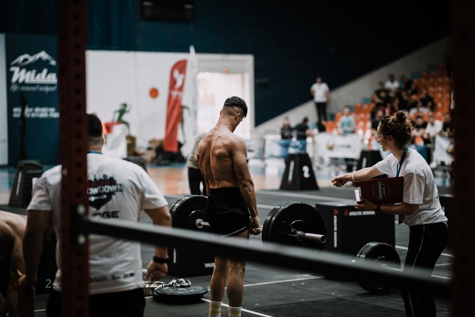 A weightlifting athlete prepares for a lift during a competition with judges observing.