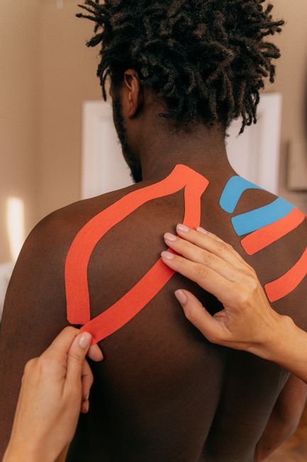 Close up of kinesio tape application on a man's shoulder for pain relief therapy.