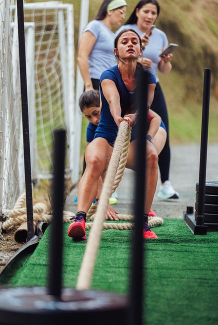 Group of women participating in a strength-training rope pull outside.