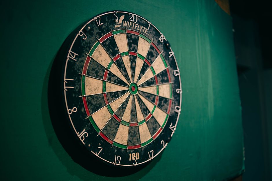 Worn dartboard on a green wall indoors, perfect for sports entertainment themes.