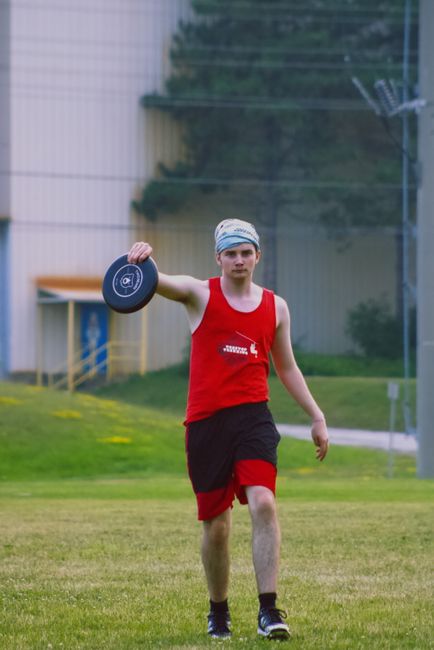 A young man in athletic wear playing frisbee outdoors in a park setting.