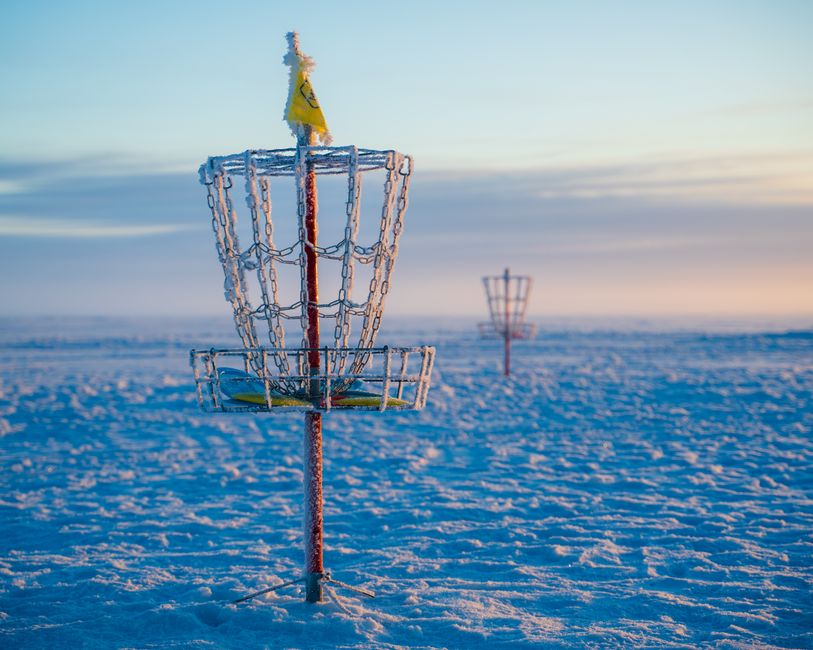 Frosty disc golf basket in a snowy open field during a winter sunrise, capturing serene outdoor vibes.