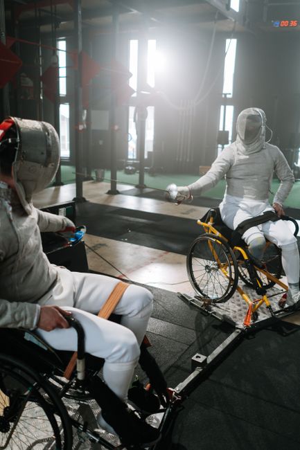 Two wheelchair fencers compete indoors, showcasing adaptive sports.