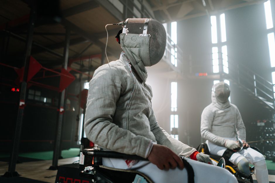 Fencing athletes in wheelchairs practicing in a modern indoor sports facility.