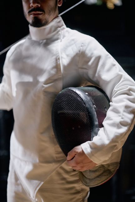 Close-up of a fencer in gear holding a mask, highlighting sport and technique.
