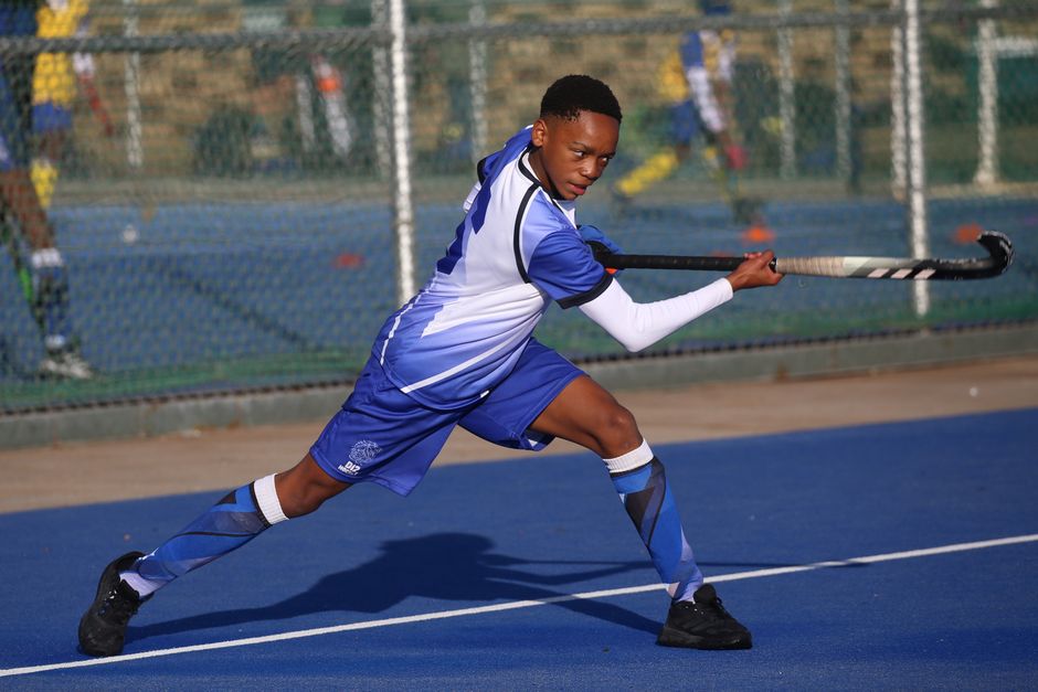 Young male athlete performing a powerful field hockey stroke on a vibrant blue field.